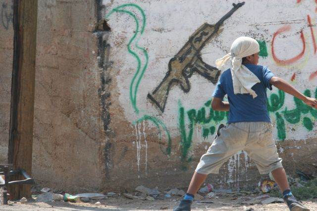 A boy sprays graffiti of an M16 — camp walls